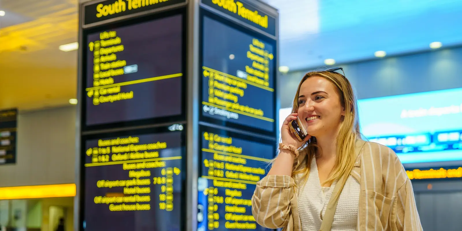 Reisende telefoniert neben einer Abflugtafel am Flughafen mit mehreren Ländern