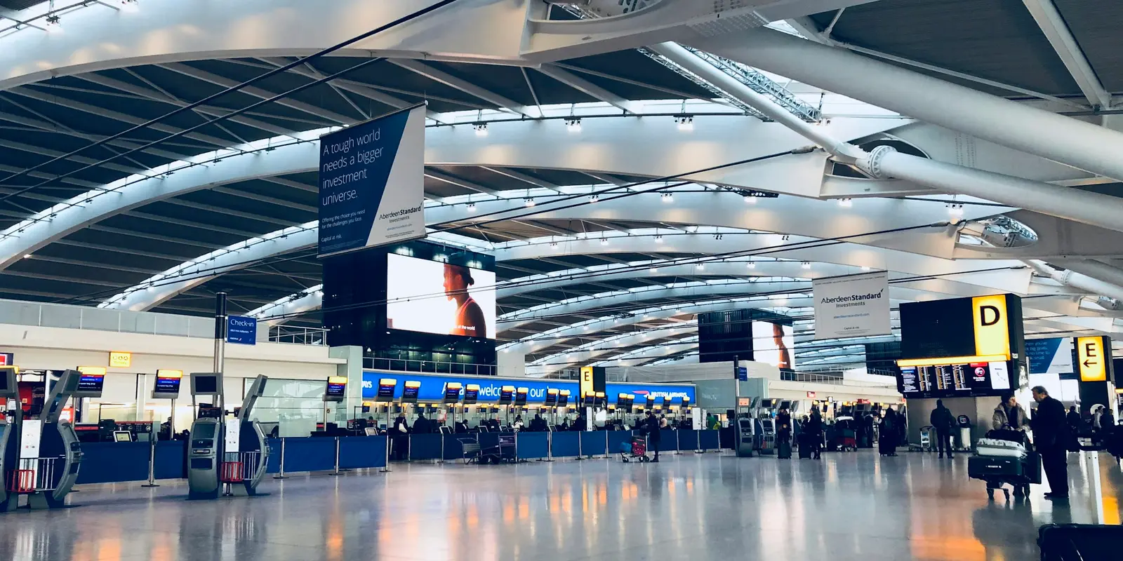 A Heathrow-style departure hall — check-in and waiting areas are covered by _Heathrow Wi-Fi Rows of travelers waiting in a departure area with luggage at an airport terminal