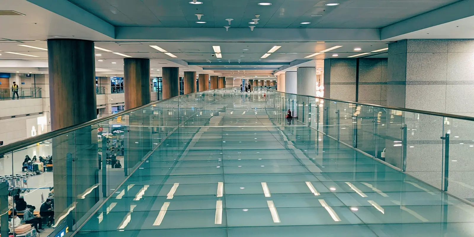 A modern indoor walkway with a glass floor and ceiling lights inside Incheon International Airport's passenger terminal